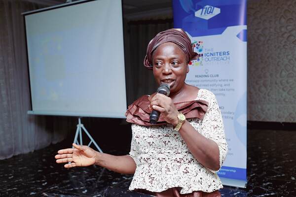 A woman speaking into a microphone beside a projector screen