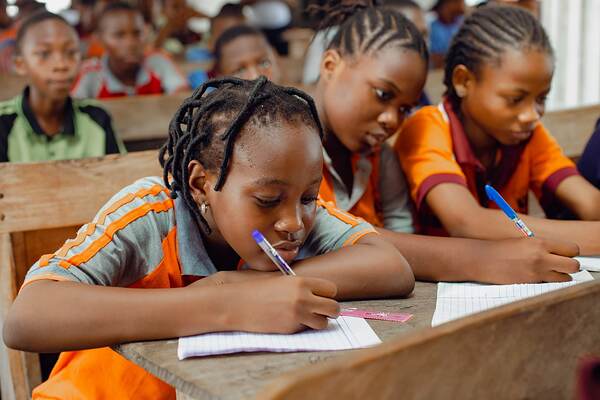 Students writing at a shared desk, heads down
